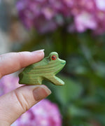 An Ostheimer Wooden green sitting frog Figure held in an adult's hand for scale. 