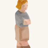 A wooden Ostheiner Hansel figure with brown hair wearing a blue jumper and brown trousers on a cream background.