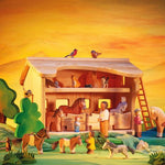 Ostheimer wooden toy Horse Stable placed in a small world play scene. The scene has lots of Ostheimer animal figures along with people and greenery and trees. 