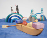  An Ostheimer lifeboat placed on blue material. There is a Santa peg doll in the boat along with wooden gifts. 