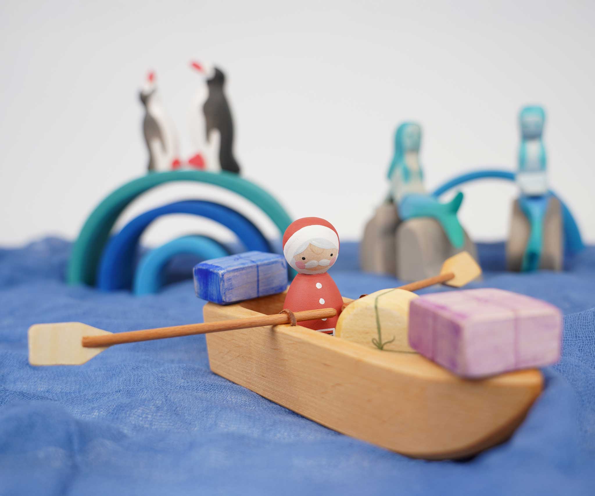 An Ostheimer lifeboat placed on blue material. There is a Santa peg doll in the boat along with wooden gifts. 