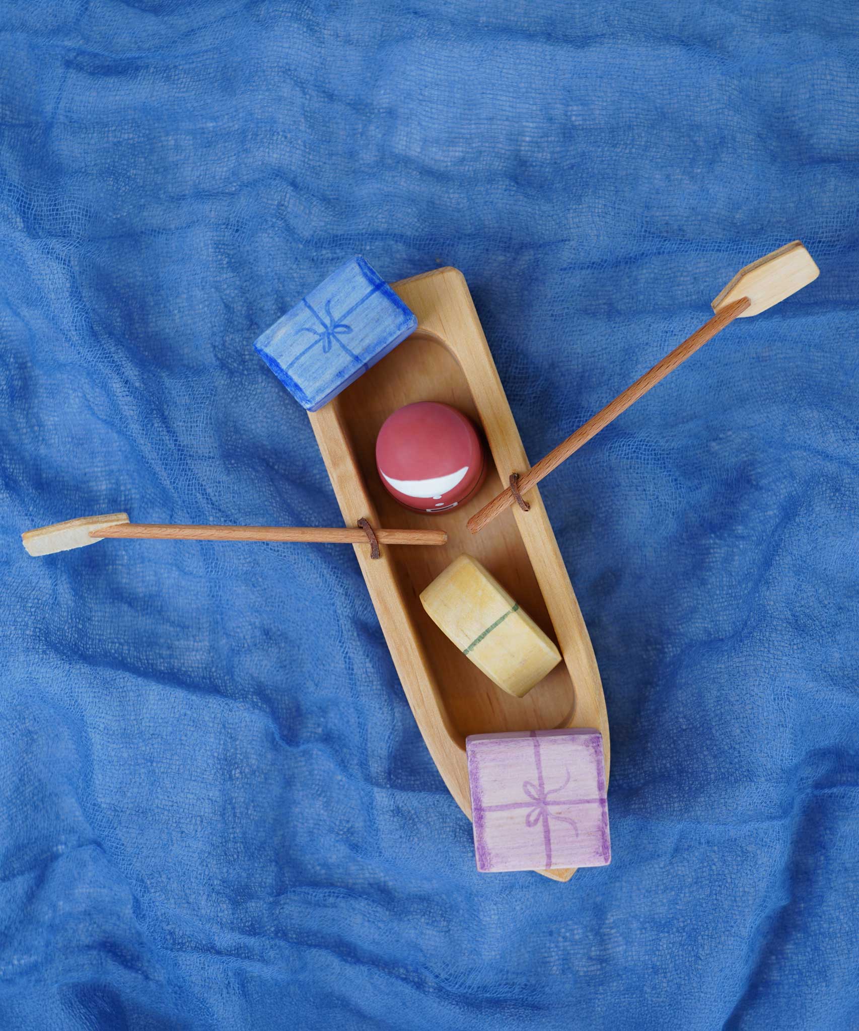 An overhead view of the Ostheimer lifeboat placed on a piece of blue material. There is a red peg doll and gifts in the lifeboat.
