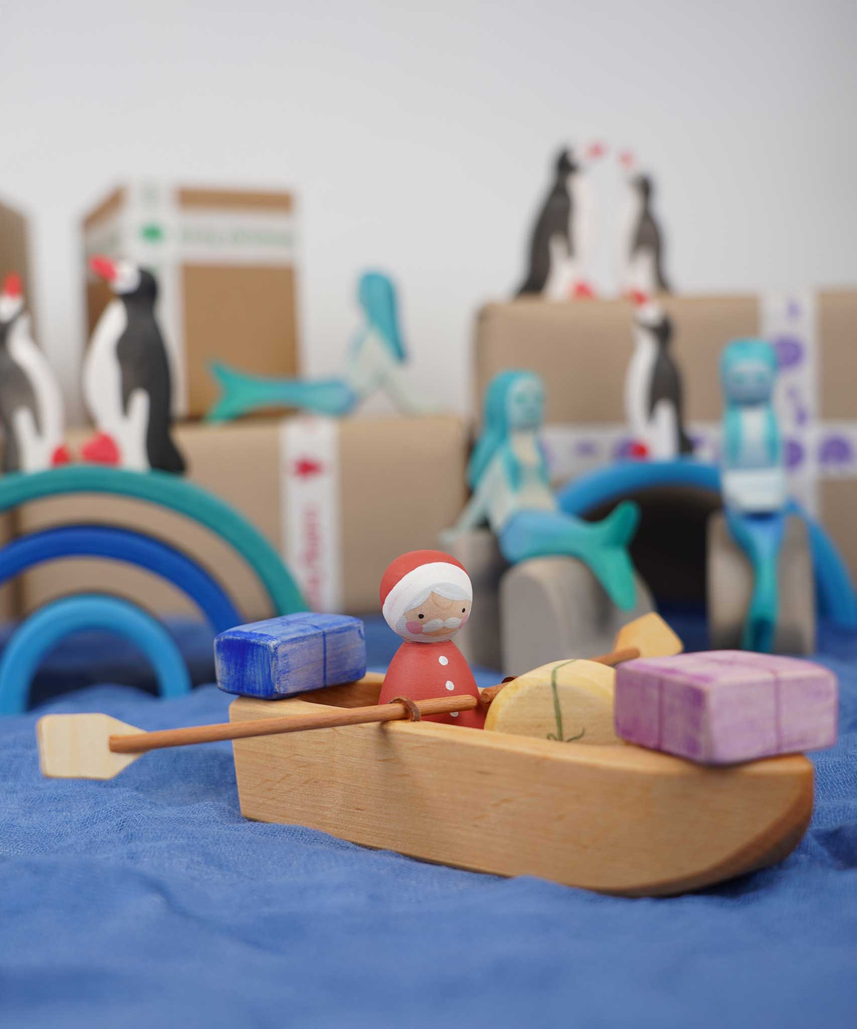  An Ostheimer lifeboat placed on blue material. There is a Santa peg doll in the boat along with wooden gifts. 
