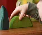 Child's hand on the Ostheimer light green wooden bush scenery piece placed on a wooden surface. 
