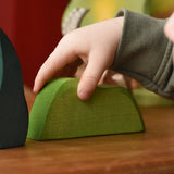 Child's hand on the Ostheimer light green wooden bush scenery piece placed on a wooden surface. 