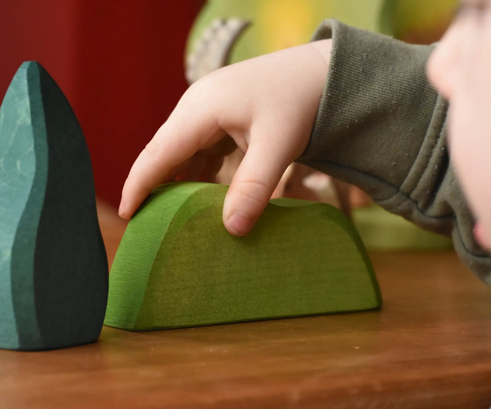 Child's hand on the Ostheimer light green wooden bush scenery piece placed on a wooden surface. 