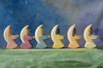 A side profile view of a host of little Ostheimer angels placed in a line on an Ostheimer pond piece. These little angel figures all have different coloured dresses, white, yellow, orange, purple, pink and blue with moon shaped wings.