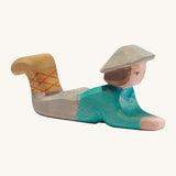 A lying wooden Ostheimer shepherd figure wearing a blue top, grey trousers and a grey hat on a cream background.