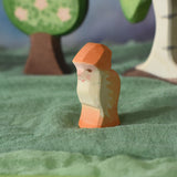 An Ostheimer orange dwarf wooden toy figure placed in a small world play scene. The dwarf figure has an orange coloured outfit with matching hat and a long white beard. The figure has been placed on a green coloured Ostheimer play scarf. This wooden figure is part of a large range of expertly hand crafted, Waldorf inspired, wooden toys here at Babipur. 