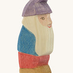 A wooden Ostheimer Paule dwarf figure wearing a blue top, red trousers and a purple hat  on a cream background
