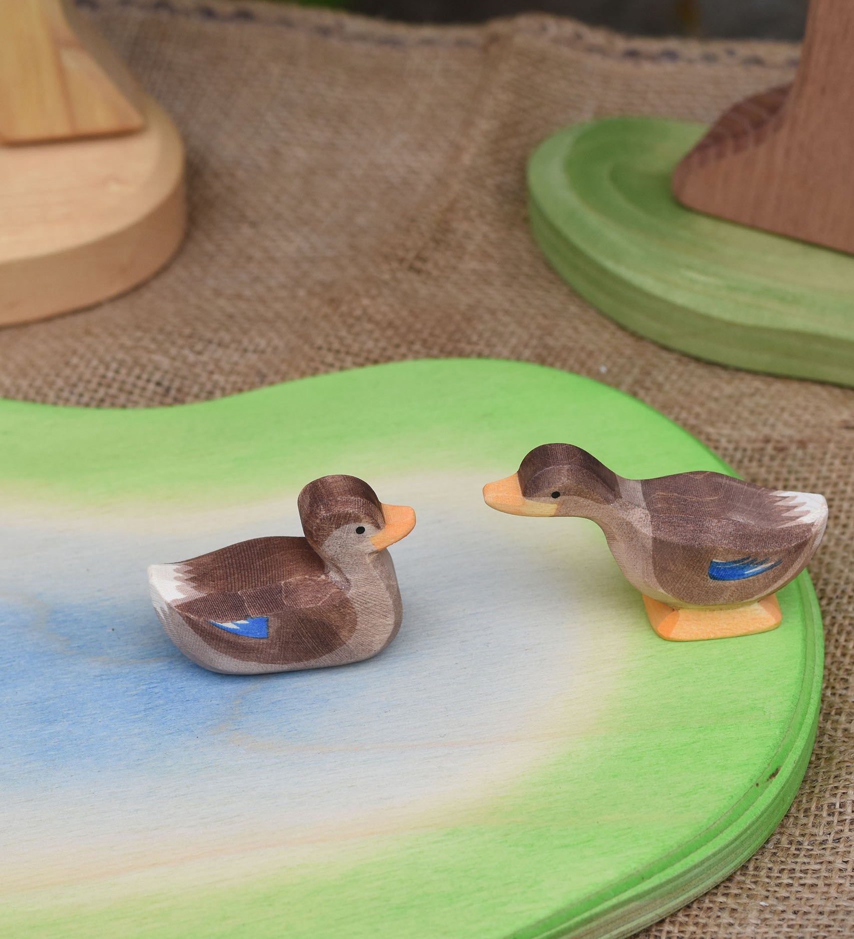 Two Ostheimer duck figures placed on a wooden pond scenery piece. 