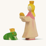 A wooden Ostheimer princess figure wearing a pink dress standing next to a king frog figure on a cream background.