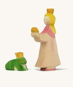 A wooden Ostheimer princess figure wearing a pink dress standing next to a king frog figure on a cream background.