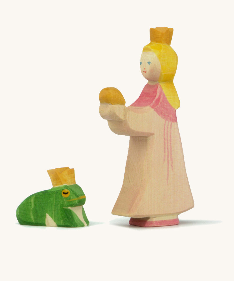 A wooden Ostheimer princess figure wearing a pink dress standing next to a king frog figure on a cream background.