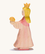A wooden Ostheimer princess wearing a pink dress with a gold crown on her head . An Ostheimer pink princess for frog prince wooden toy figure held up in an adult's hand to show scale. This wooden figure is part of a large range of expertly hand crafted, Waldorf inspired, wooden toys here at Babipur. 