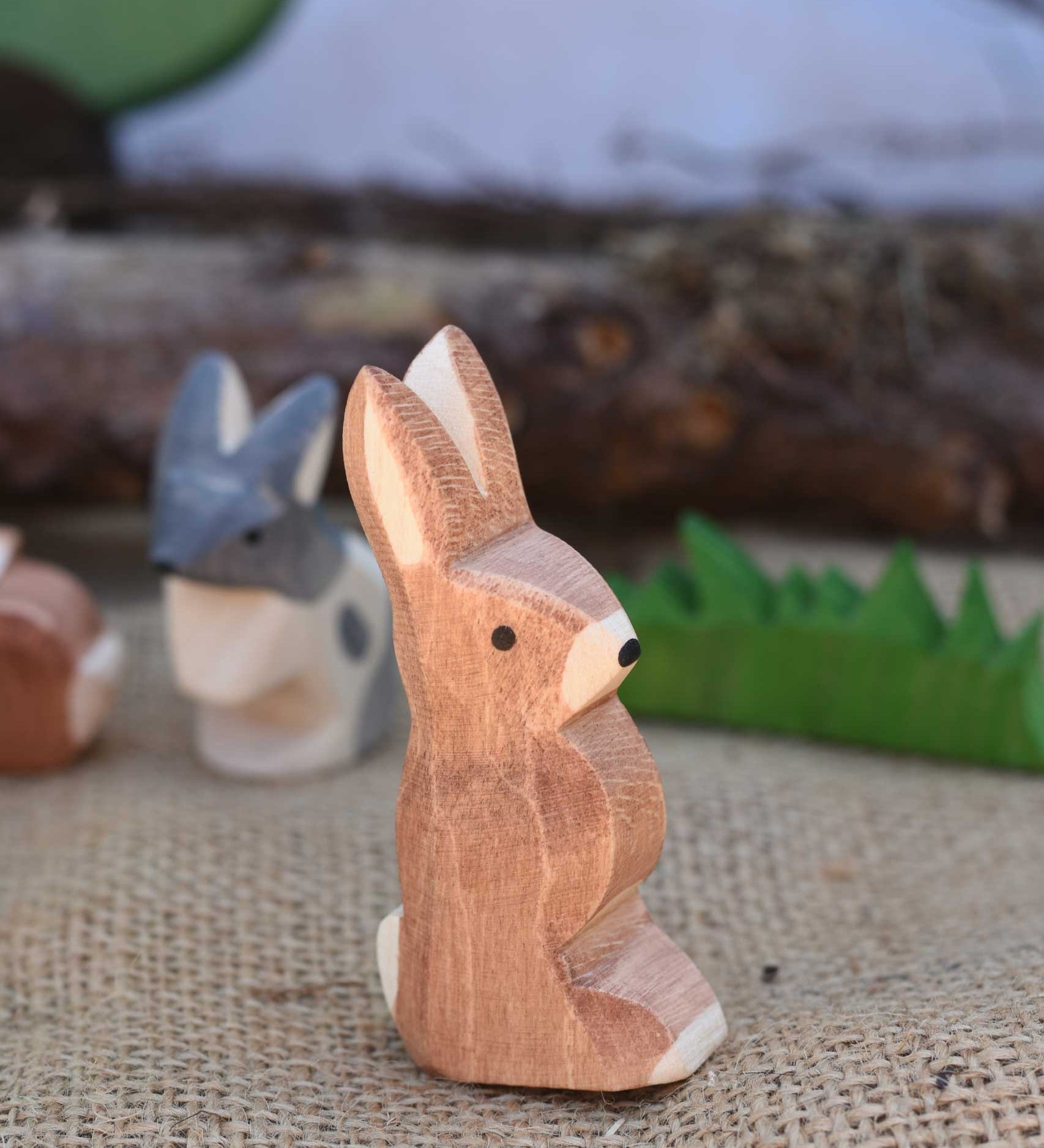 An Ostheimer wooden rabbit figure with it's ears up placed in a small world play scene. We have a full range of expertly crafted wooden toy figures and scenery available here at Babipur.