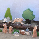 A small world play scene featuring various Ostheimer rabbit figures, green grass figures and Ostheimer trees in the background.  Check out our full range of expertly crafted wooden toy figures and scenery here at Babipur.