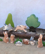 A small world play scene featuring various Ostheimer rabbit figures, green grass figures and Ostheimer trees in the background.  Check out our full range of expertly crafted wooden toy figures and scenery here at Babipur.