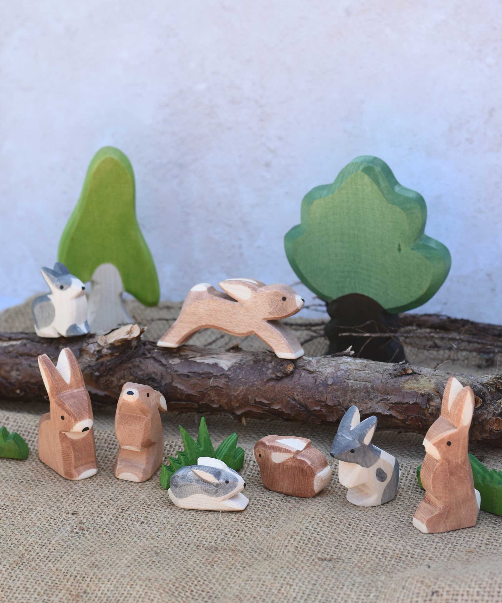 A small world play scene featuring various Ostheimer rabbit figures, green grass figures and Ostheimer trees in the background.  Check out our full range of expertly crafted wooden toy figures and scenery here at Babipur.