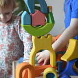 Ostheimer Rainbow Castle Blocks in a wooden tray placed on a wooden stool with children playing in the background. 