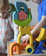 Ostheimer Rainbow Castle Blocks in a wooden tray placed on a wooden stool with children playing in the background. 