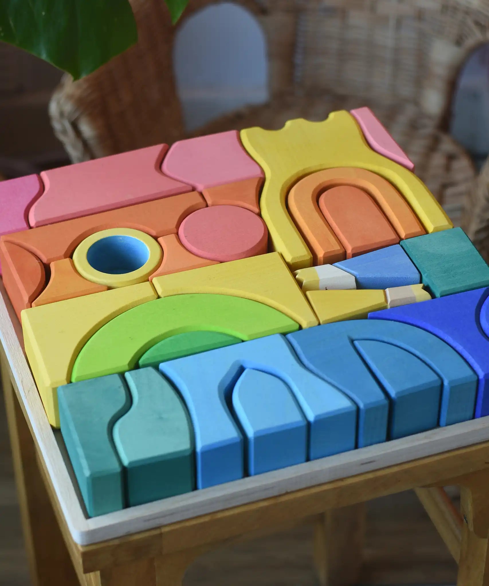 Close up of the Ostheimer Rainbow Castle Blocks in a wooden tray placed on a wooden stool. 