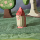 An Ostheimer red dwarf wooden toy figure placed in a small world play scene. The dwarf figure has a red coloured outfit with matching hat and a long white beard. The figure has been placed on a green coloured Ostheimer play scarf. This wooden figure is part of a large range of expertly hand crafted, Waldorf inspired, wooden toys here at Babipur. 