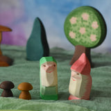 Two Ostheimer dwarves wooden toy figures placed in a small world play scene. The dwarf figures have red and green coloured outfits with matching hats and a long white beard. The figures have been placed on a green coloured Ostheimer play scarf. These wooden figures are part of a large range of expertly hand crafted, Waldorf inspired, wooden toys here at Babipur. 