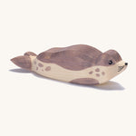 A wooden resting Ostheimer sea lion figure on a cream background.