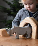 The large Ostheimer rhino wooden toy figure placed on a wooden surface. A child can be seen looking on excitedly in the background. These wooden figures are part of a wide range of expertly hand crafted wooden toys here at Babipur.