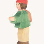 A wooden Ostheimer shepherd boy figure weaing a green coat, brown trousers and a red hat on a cream background.