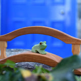 An Ostheimer Wooden sitting frog Figure placed on a wooden bridge toy on a stone wall outdoors. 