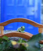 An Ostheimer Wooden sitting frog Figure placed on a wooden bridge toy on a stone wall outdoors. 