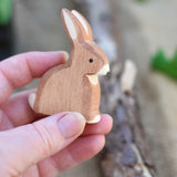 An Ostheimer wooden toy rabbit shown in an adult's hand for scale. Check out our full range of expertly crafted wooden toy figures and scenery here at Babipur.