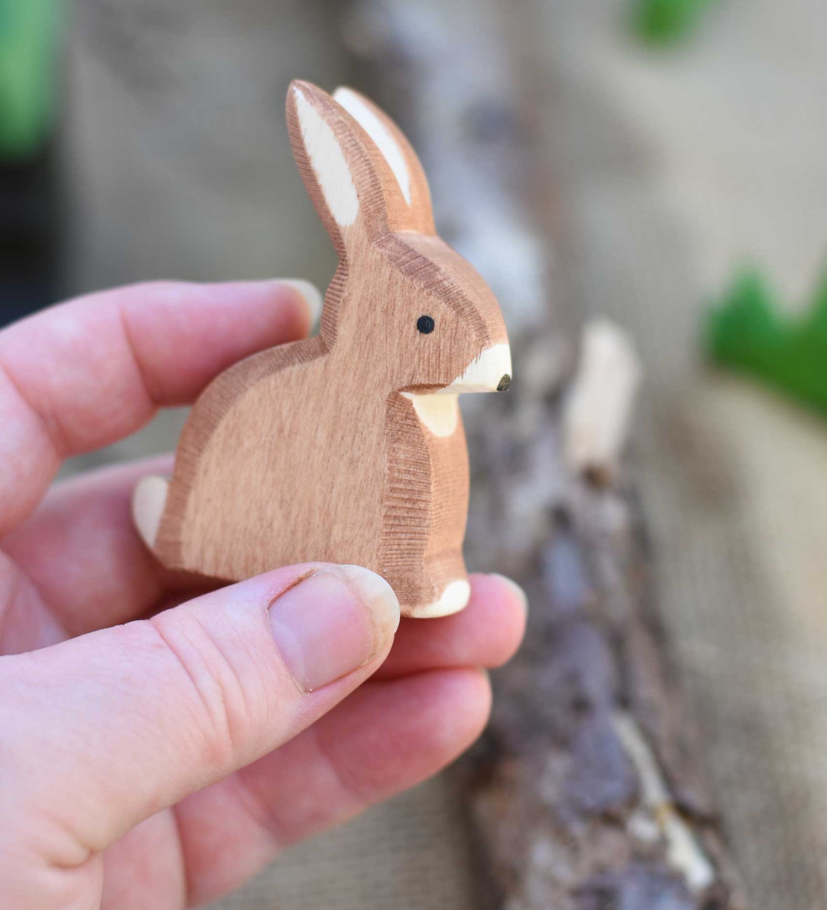 An Ostheimer wooden toy rabbit shown in an adult's hand for scale. Check out our full range of expertly crafted wooden toy figures and scenery here at Babipur.