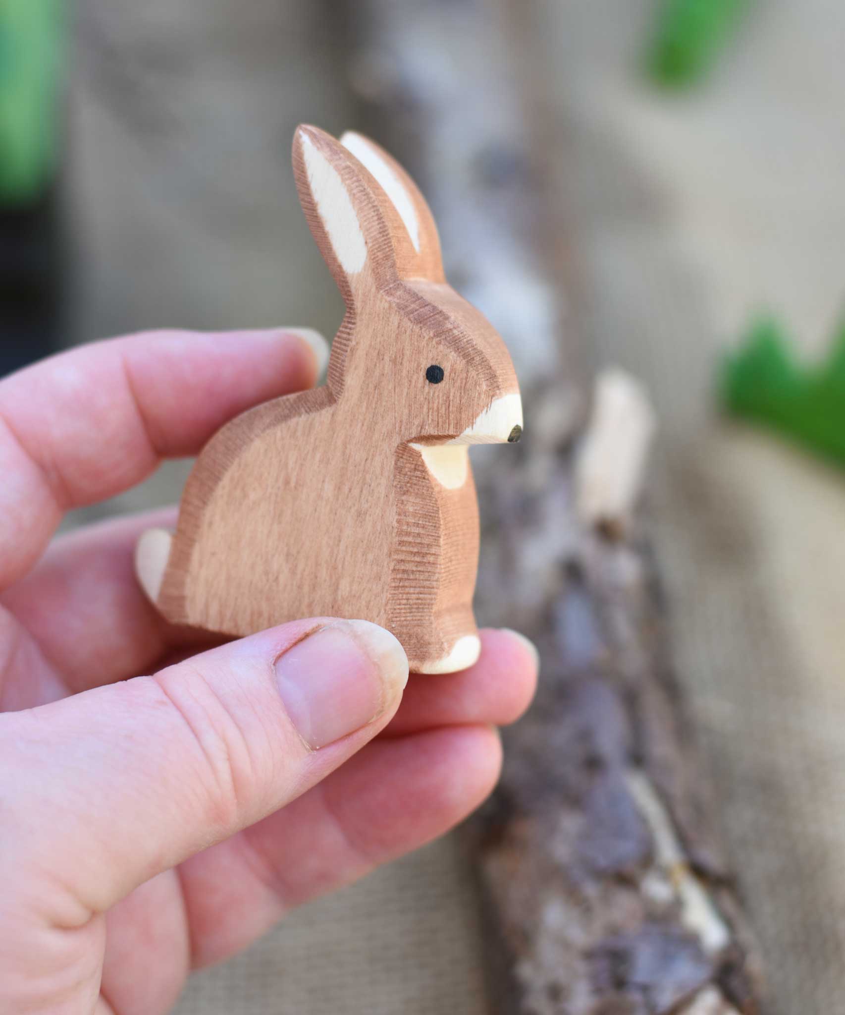 An Ostheimer wooden toy rabbit shown in an adult's hand for scale. Check out our full range of expertly crafted wooden toy figures and scenery here at Babipur.