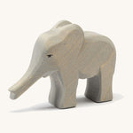 A small wooden Ostheimer elephant figure with its trunk out on a cream background.