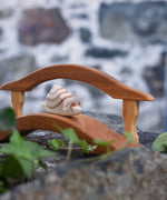 An Ostheimer wooden snail figure placed on the Ostheimer wooden bridge with railing. These wooden toys are part of a wide range of Ostheimer figures available at Babipur.