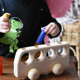 Close up of a child playing with the Ostheimer Natural Bus With 4 People. The child is placing the blue coloured wooden people figure into one of the slots at the top of the bus. 