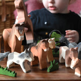 Child playing with a collection of Ostheimer wooden toy horse figures with green grass scenery pieces.