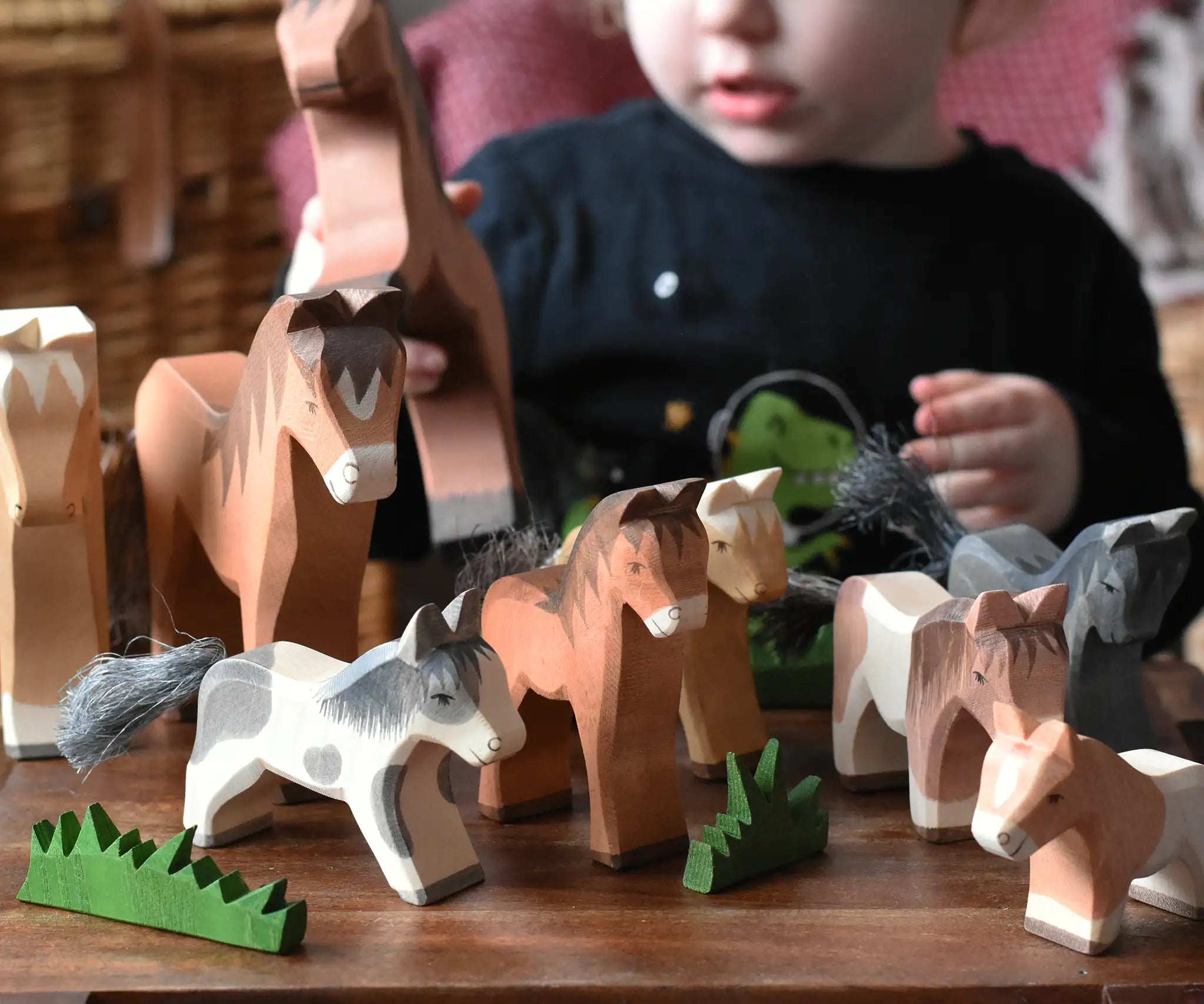 Child playing with a collection of Ostheimer wooden toy horse figures with green grass scenery pieces.
