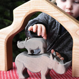 The small Ostheimer rhino wooden toy figure stacked on top of the large rhino. A child can be seen reaching for the rhinos in the background. These wooden figures are part of a wide range of expertly hand crafted wooden toys here at Babipur.