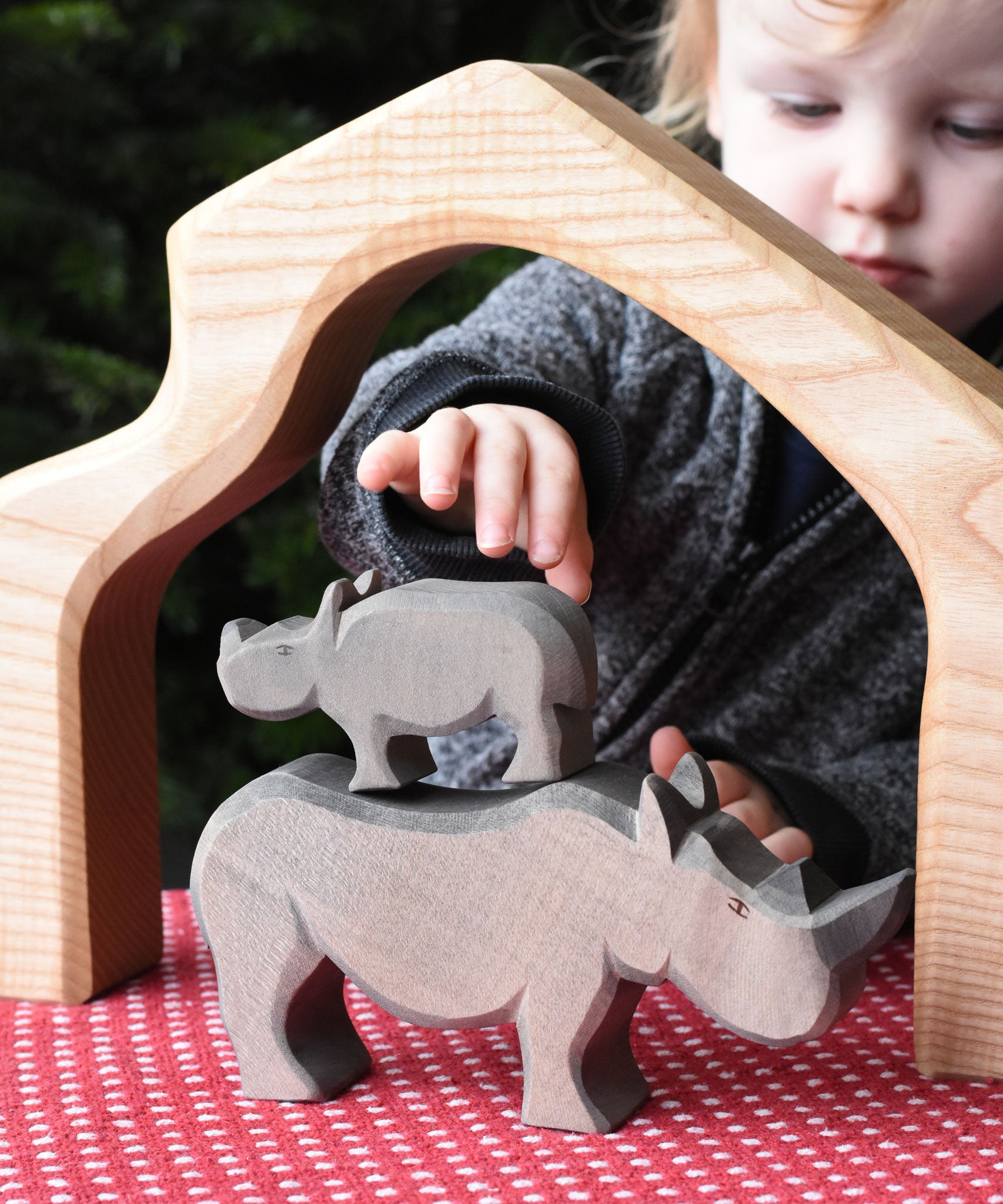 The small Ostheimer rhino wooden toy figure stacked on top of the large rhino. A child can be seen reaching for the rhinos in the background. These wooden figures are part of a wide range of expertly hand crafted wooden toys here at Babipur.