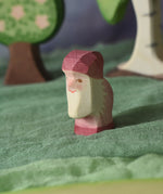 An Ostheimer violet dwarf wooden toy figure placed in a small world play scene. The dwarf figure has a violet coloured outfit with matching hat and a white beard. The figure has been placed on a green coloured Ostheimer play scarf. These wooden figures are part of a large range of expertly hand crafted, Waldorf inspired, wooden toys here at Babipur.