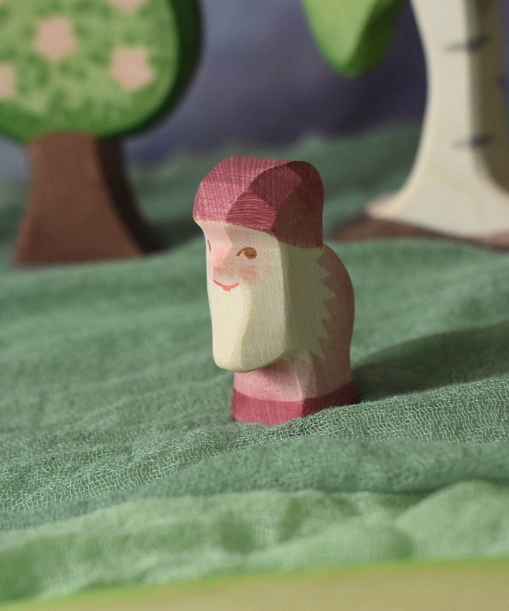 An Ostheimer violet dwarf wooden toy figure placed in a small world play scene. The dwarf figure has a violet coloured outfit with matching hat and a white beard. The figure has been placed on a green coloured Ostheimer play scarf. These wooden figures are part of a large range of expertly hand crafted, Waldorf inspired, wooden toys here at Babipur.