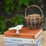An Ostheimer wagtail wooden bird figure placed on top of a pile of old books next to a Kraul basket.