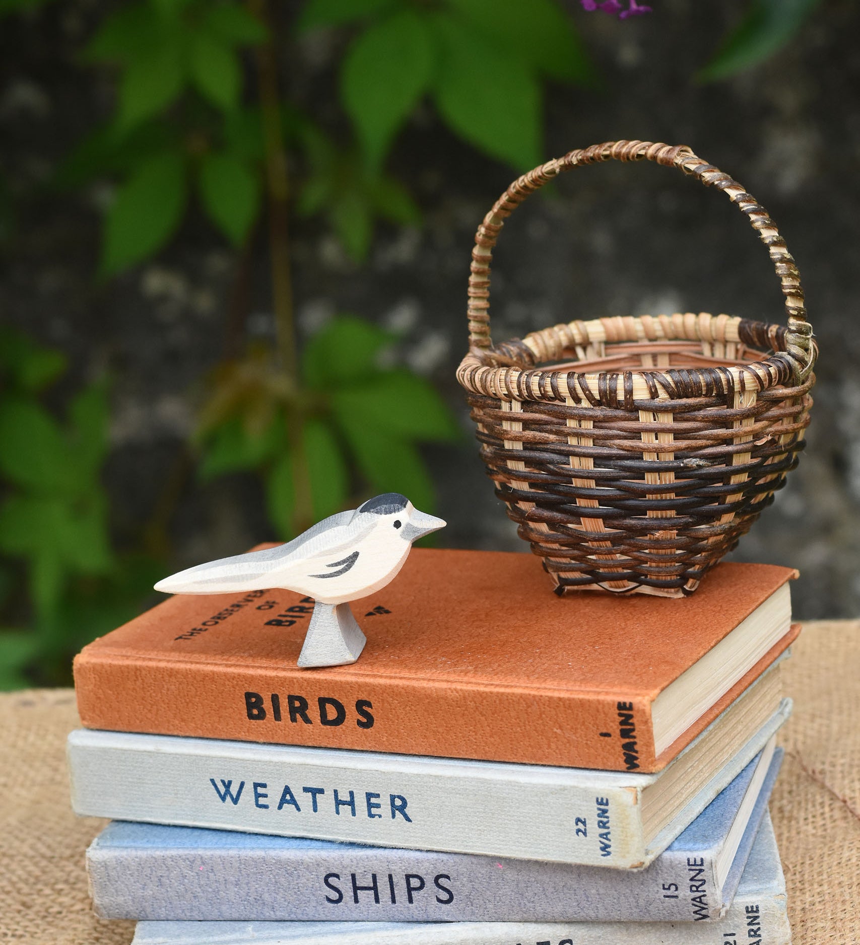 An Ostheimer wagtail wooden bird figure placed on top of a pile of old books next to a Kraul basket.