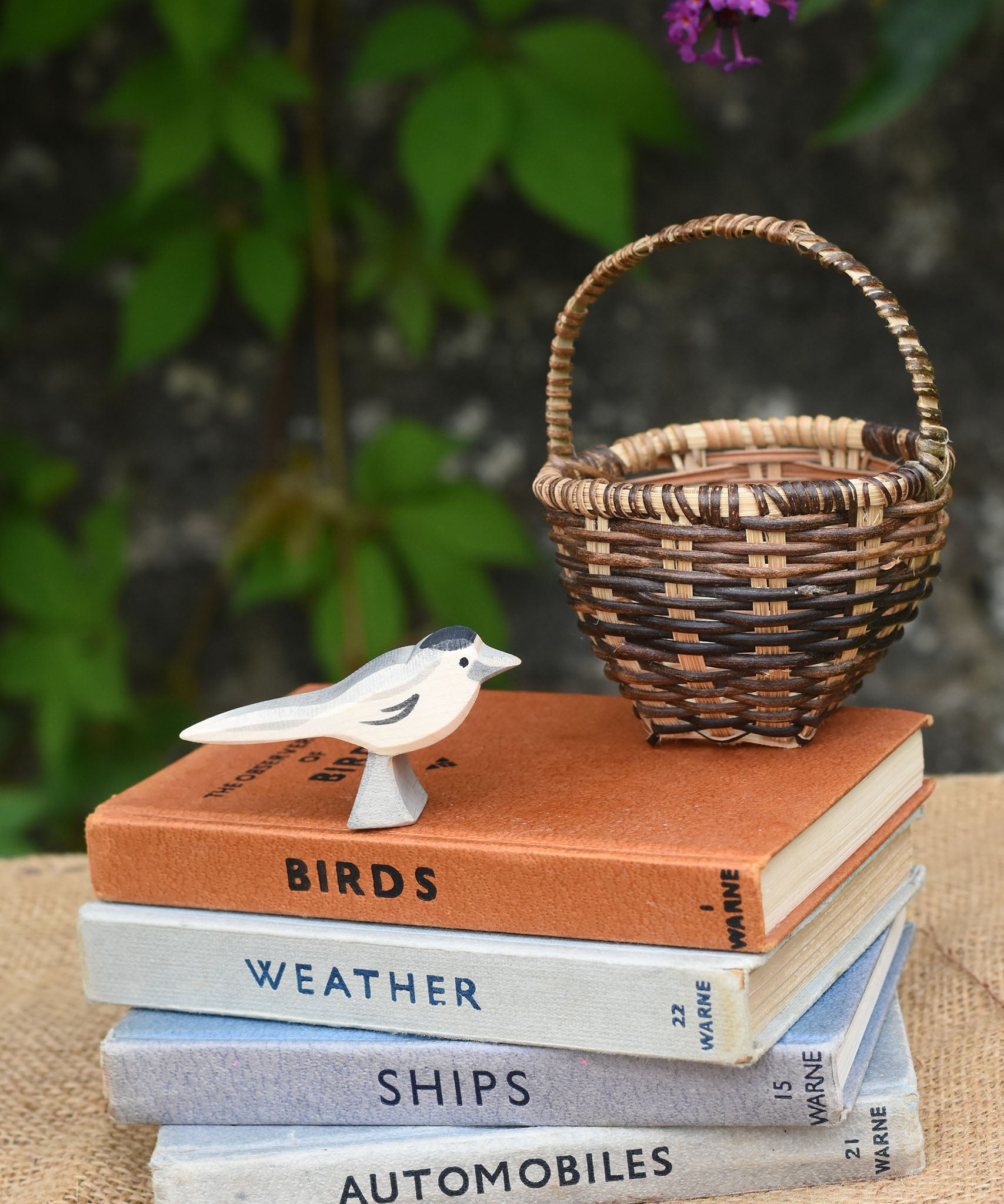 An Ostheimer wagtail wooden bird figure placed on top of a pile of old books next to a Kraul basket.