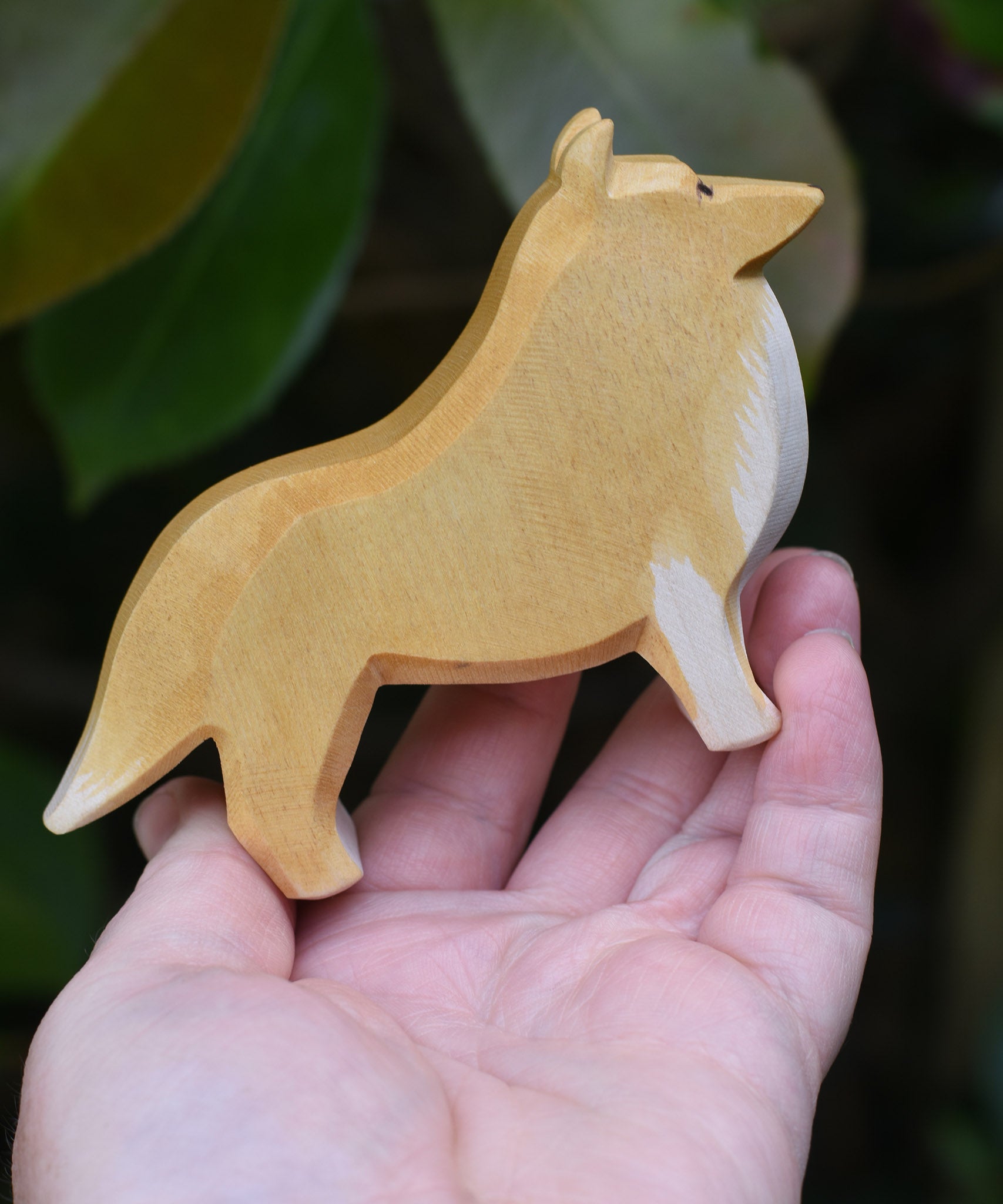 An Ostheimer Collie Dog Handmade Wooden Toy in an adults hand. These wooden figures are part of a large range of expertly hand crafted, Waldorf inspired, wooden toys here at Babipur.