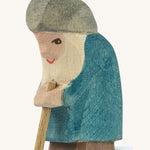A wooden Ostheimer Willi dwarf figure wearing a blue coat and a grey hat holding a wooden staff on a cream background.